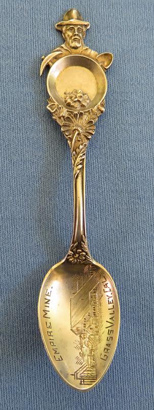 Souvenir Mining Spoon Empire Mine Grass Valley CA.JPG - SOUVENIR MINING SPOON EMPIRE MINE GRASS VALLEY CA - Sterling silver souvenir spoon,  features  handle with figural miner behind pan with gold nuggets and pick and shovel, flower with deep relief decoration down the handle, bowl has engraved image of mining scene, marking  is EMPIRE MINE, GRASS VALLEY, CAL., measures 4" in length , reverse marked STERLING with hallmark  of H on a pennant for Mechanics Sterling Company, which was subsidiary of Watson Newell Co. [The city of Grass Valley is the largest city in the western region of Nevada County, California.  Situated at roughly 2,500 feet elevation in the western foothills of the Sierra Nevada mountain range, this historic northern Gold Country city is 57 miles north by northeast  from the state capitol in Sacramento. Grass Valley, which was originally known as Boston Ravine and later officially named Centerville, dates from the California Gold Rush, as does nearby Nevada City. When a post office was established in 1851, it was renamed Grass Valley the following year.   The town incorporated in 1860. Grass Valley is the location of the Empire Mine and North Star Mine, two of the oldest, largest, deepest, longest and richest gold mines in California.  Many of those who came to settle in Grass Valley were tin miners from Cornwall, England. They were attracted to the California gold fields because the same skills needed for deep tin mining were needed for hard rock (deep) gold mining. Many of them specialized in pumping the water out of very deep mining shafts.  George Roberts identified the Ophir Hill vein, which would eventually become the Empire Mine, which along with the Northstar Mine and the Idaho Maryland Mine would eventually produce nearly $300 million worth of gold. The Northstar and Idaho Maryland mines are discussed elsewhere in my Souvenir Mining Spoons pics.   Roberts founded the Empire mine in 1851. In 1852, the mine was purchased by the Empire Mining Company, which maintained mines throughout the area. Controlling interest of the mine changed hands several times throughout the 1850s, when many of the individual placer miners began to flee for Virginia City, Nev., looking to cash in on Nevada's burgeoning Silver Rush.  By 1869, William Bourn Sr. procured controlling interest in the company and the Bourn family would maintain control of the mine until 1929, when they sold it to Newmont Mining.  When Bourn Sr. died in 1874, his namesake, William Bourn Jr., assumed operation of the mine that most engineers believed had been picked clean over the past decades. Undaunted, Bourn Jr., just 21 years old at the time, poured money into exploration of the underground workings, that within four years continued to yield copious amounts of gold.  With his younger cousin, George Starr in tow, the two men transformed the plodding gold producer into a world-class showcase for modern mining, utilizing the Cornish miners' technological innovation of using steam pumps to keep the underground workings dry.  At its zenith, the mine employed more than 400 miners, who would board ore cars 20 at a time and be lowered rapidly down an incline to nearly 11,000 feet below the surface. All told, the mine comprised 367 miles of underground workings.  In 1929, Bourn Jr. sold the mine to the Newmont Mining Corp. for $250,000, which operated the mine continuously until the advent of World War II, when the War Production Board forced the shutdown of the mine.  The War Production Board's decision was in stark contrast to the Abraham Lincoln's policy toward the gold mines in California during the American Civil War, as much of the precious metals that were disinterred during his administration were sold to augment The Union's coffers and bolster its war machine.  The mine opened briefly again in the 1950s, but the price of gold had plummeted so far that it was unprofitable to run the Empire Mine and it was closed for good in 1956. Between 1851 and its closure in 1956, the Empire Mine produced 5.8 million ounces of gold.  In April 1975, Newmont sold the mine to the state of California for $1.25 million and the California Parks Department transformed the nearly 800 acres of land into one of the most visited vestiges of the California Gold Rush.  The Empire Mine State Historic Park is a state-protected mine and park in Grass Valley, California.  The park is on the National Register of Historic Places, a federal Historic District, and a California Historical Landmark.]